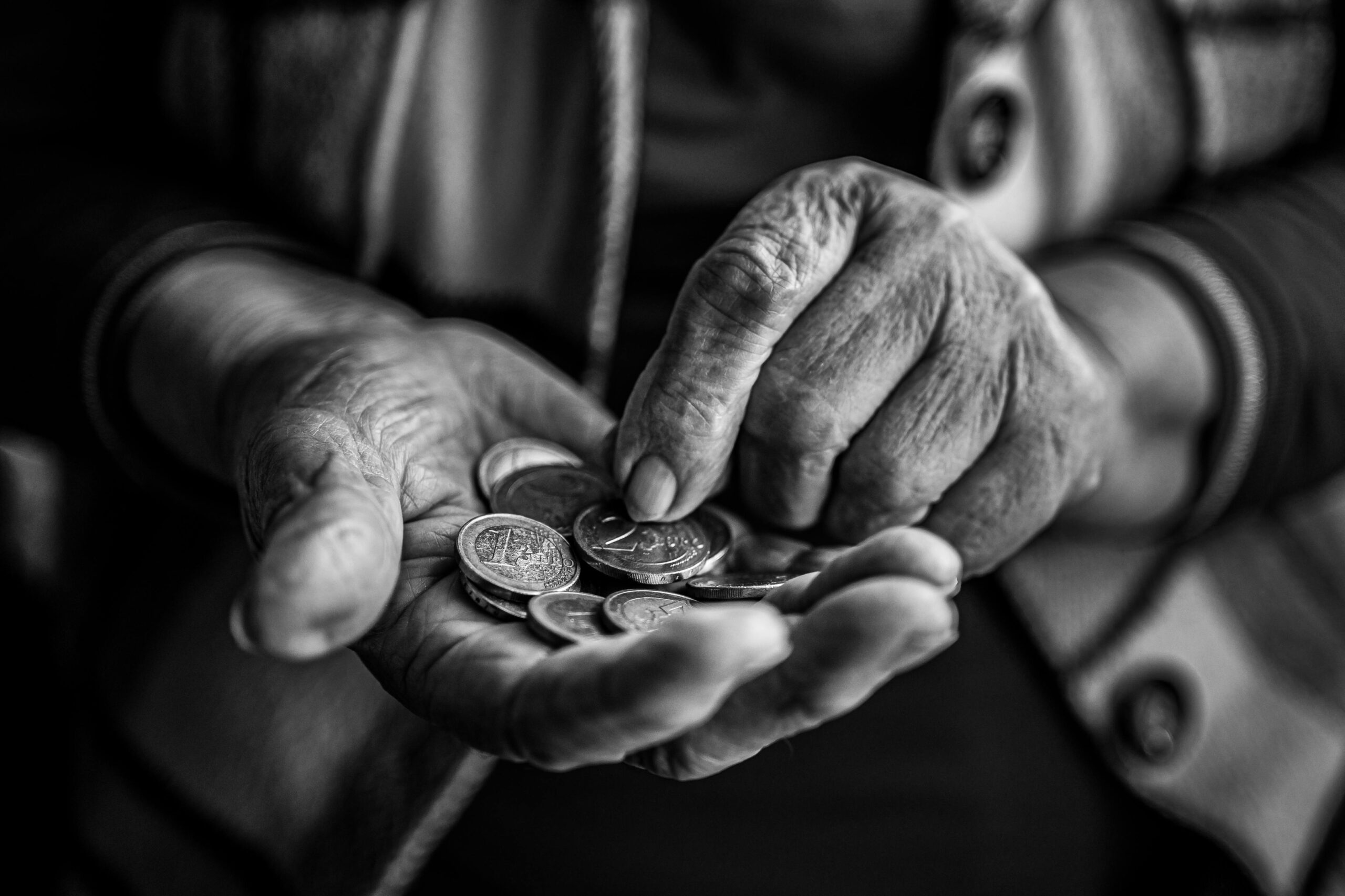 Close-up of elderly hands holding and counting coins, captured in black and white for a timeless feel.
