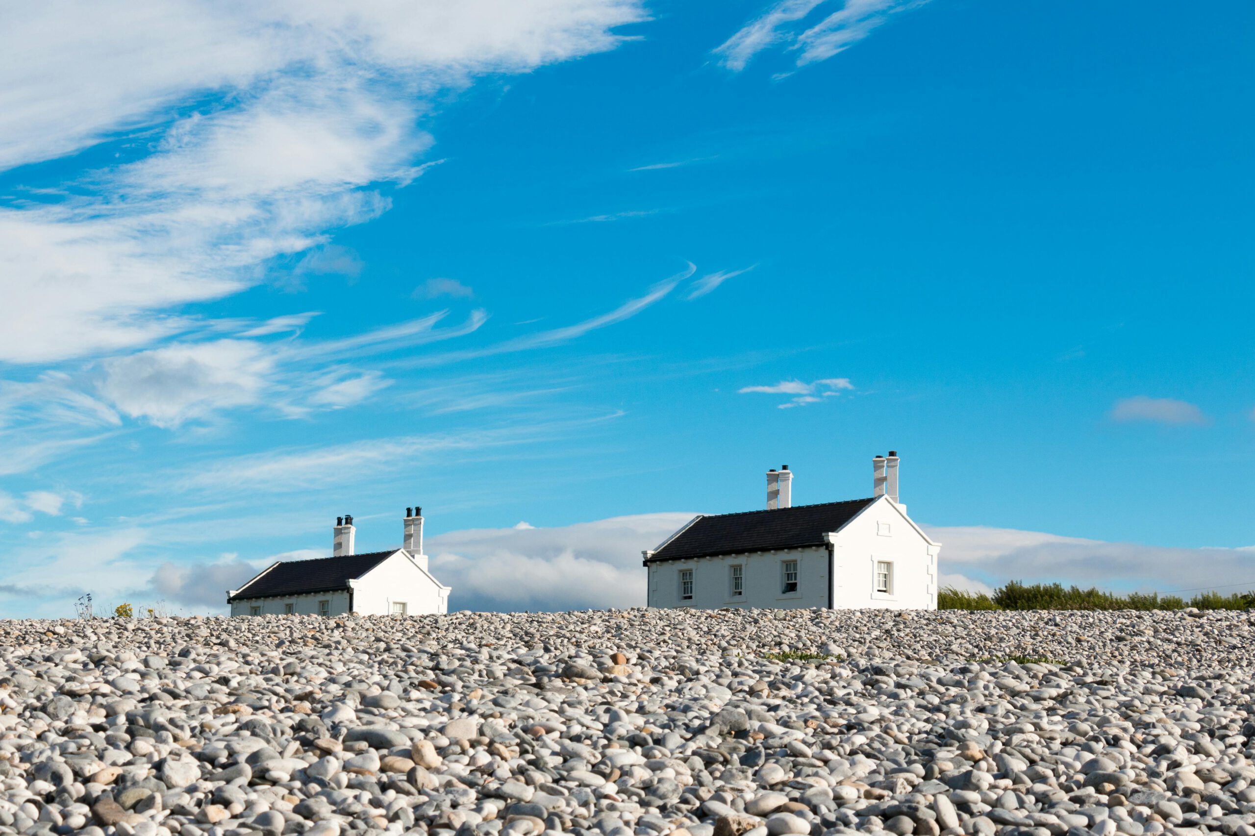 White cottages on a pebble beach under a clear blue sky in Wales.
