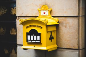 A vintage yellow mailbox against a stone wall with ornate design elements.