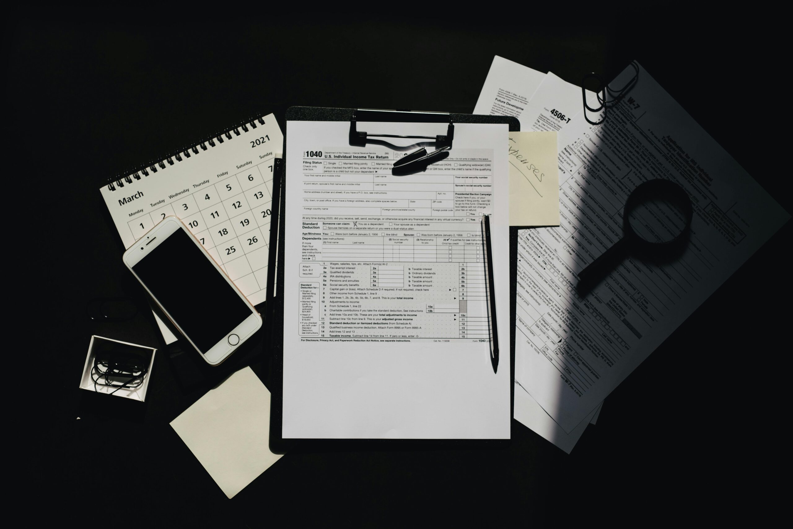 Flat lay of tax documents, calendar, and smartphone on a dark surface, symbolizing tax preparation.