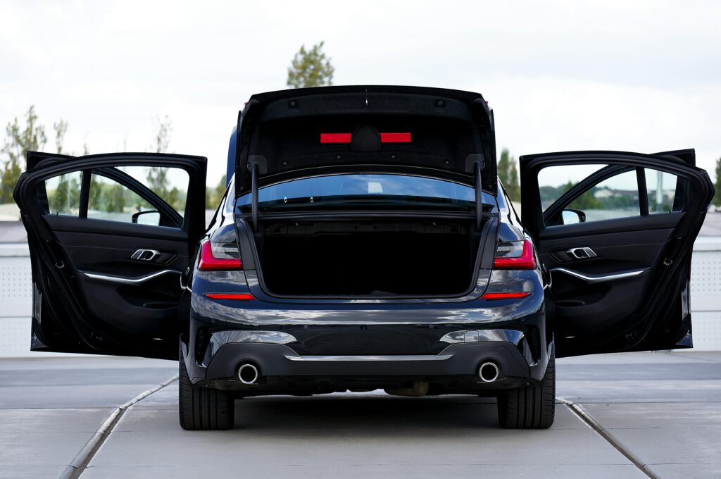 Rear view of a modern black car with open doors and trunk, showcasing its stylish design.