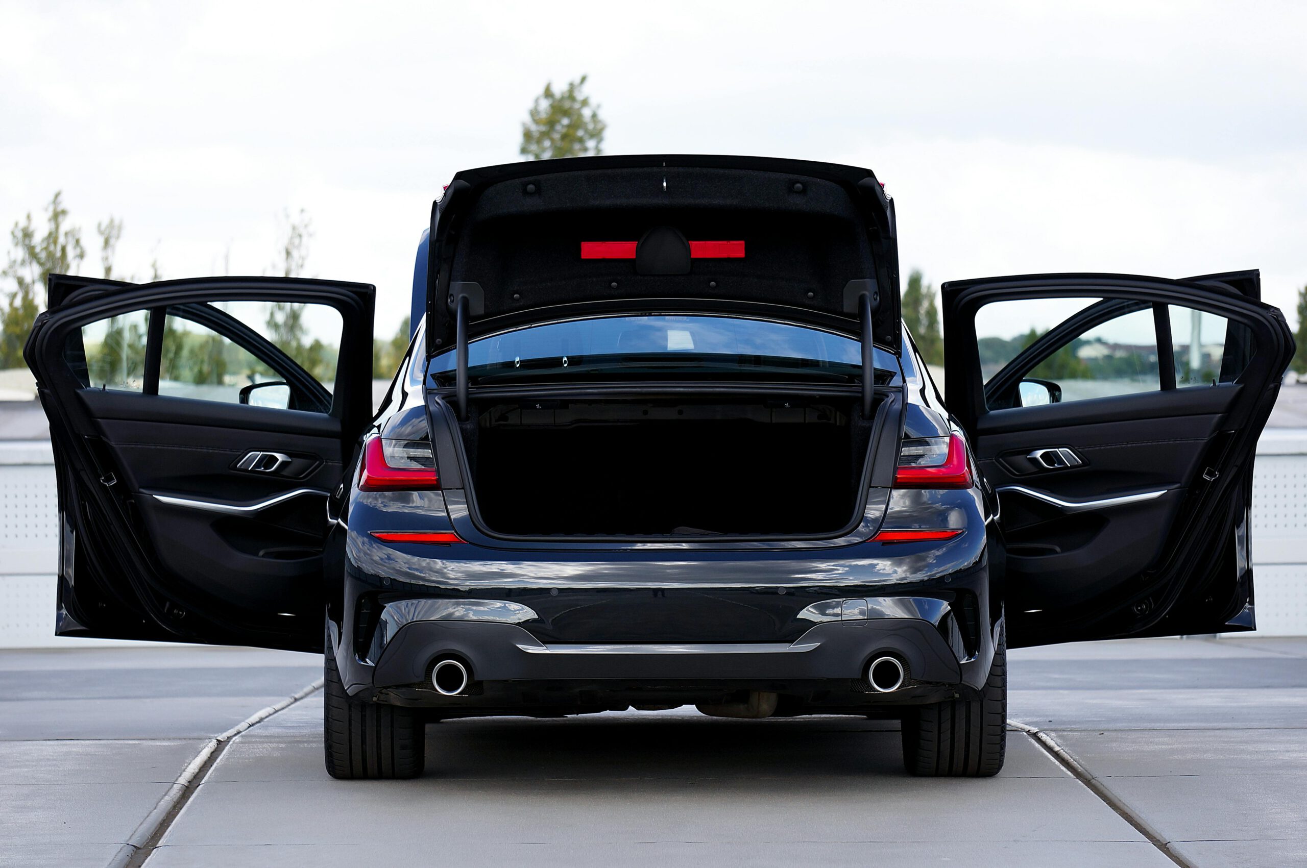 Rear view of a modern black car with open doors and trunk, showcasing its stylish design.