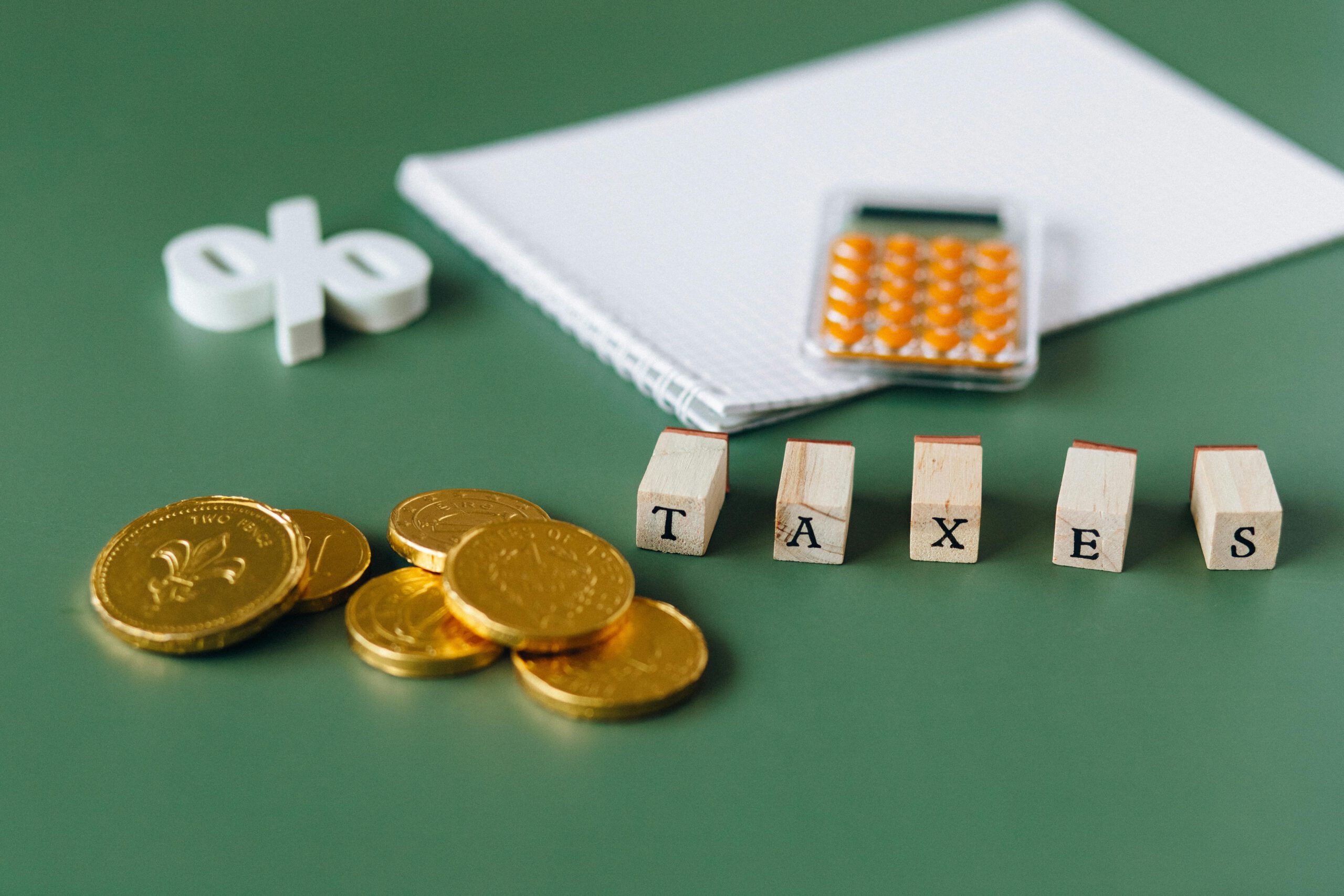 Close-up of tax-related items including coins, calculator, and word 'taxes' on a green background.