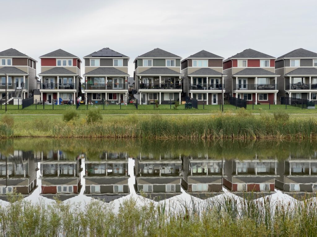 A row of modern houses reflected in a calm pond, showcasing serene suburban architecture.