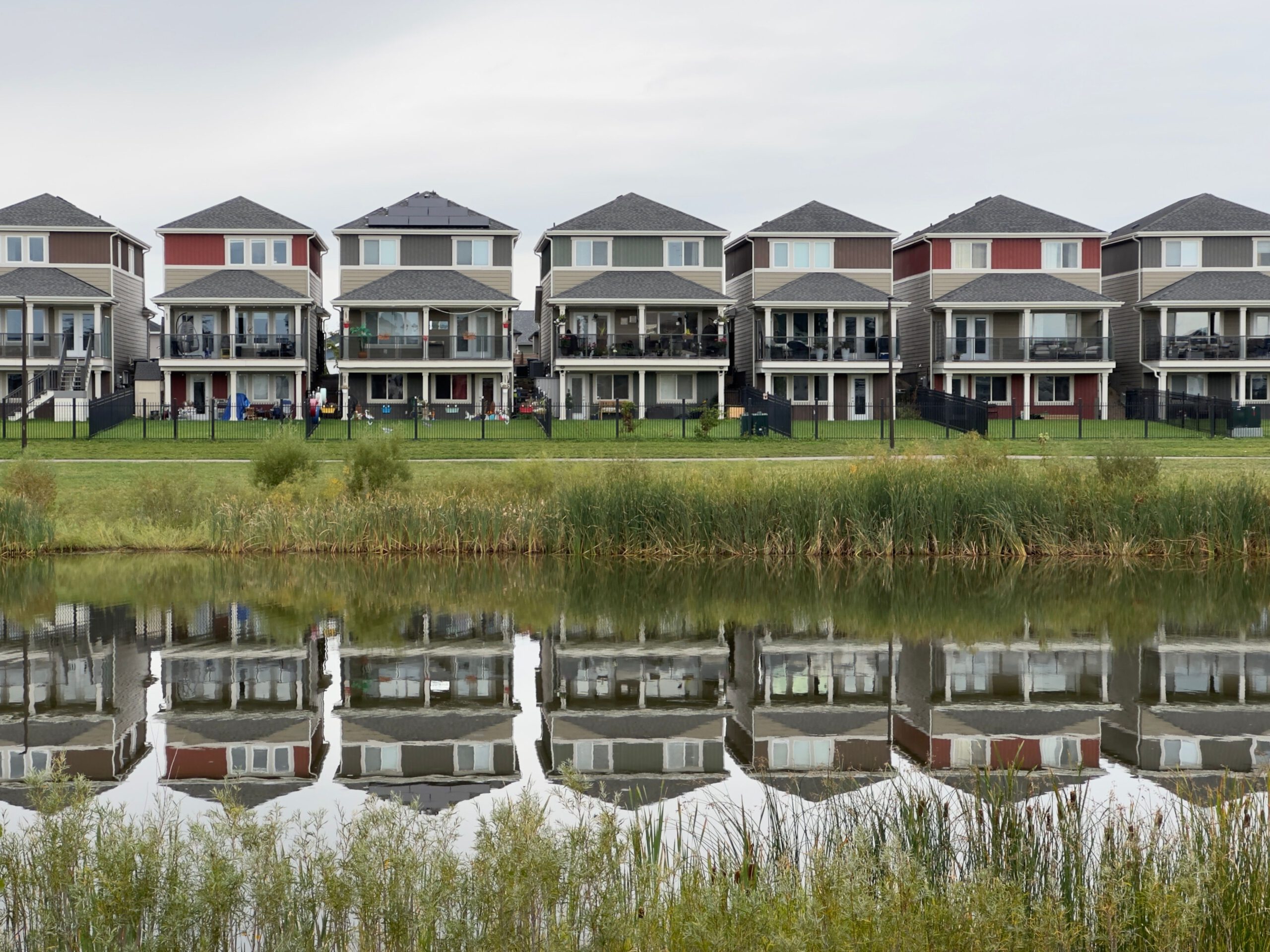 A row of modern houses reflected in a calm pond, showcasing serene suburban architecture.